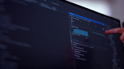 Quellcode auf einem Monitor mit zeigendem Finger im dunklen Büro