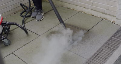 Dampfreiniger hüllt Terrassenfliesen in dichten Wasserdampf vor einer Ziegelwand