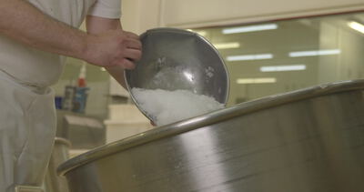 Mitarbeiter schüttet Zucker in eine industrielle Mischtrommel