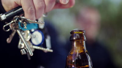 Hand öffnet eine Bierflasche mit einem Flaschenöffner am Schlüsselbund