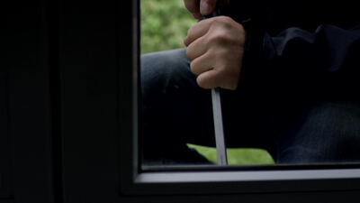 Hand mit Brecheisen hebelt ein Fenster von außen auf