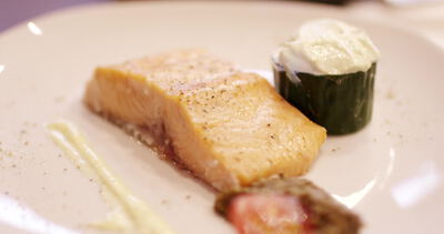 Angerichtetes Lachsfilet mit Cremenocke auf weißem Teller