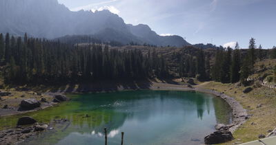 Bergsee mit Spiegelung im Gegenlicht vor dunstigem Gebirgskamm