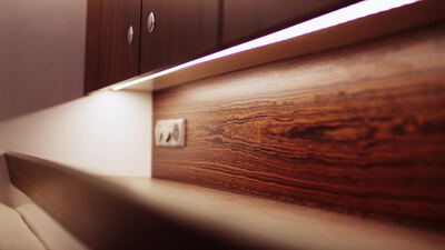 Nahaufnahme einer dunklen Holzvertäfelung mit Steckdose und Lichtband