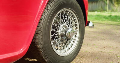 Hinteres Speichenrad eines roten Oldtimer Sportwagens am Kiesweg