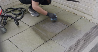 Hand wischt nach der Dampfreinigung über Terrassenfliesen neben dem fahrbaren Gerät