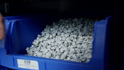Hand greift Metallteile aus einer blauen Lagerbox