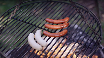 Bratwürste und Weißwürste brutzeln auf dem Schwenkgrill über offenem Feuer
