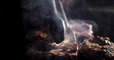 Koch wendet dicke Steaks mit der Grillzange auf dem Grill im Rauch