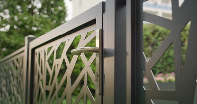Ein modernes Metalltor mit geometrischem Muster zeigt Griff und Schloss im Detail