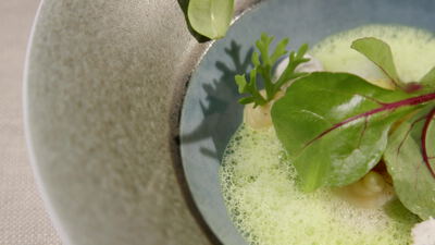 Grüne Schaumsuppe mit Kräutern in Steingutschale auf Leinen Grüne Schaumsuppe mit Kräutern in Steingutschale auf Leinen, Suppe in Schale, Kräuter auf der Suppe und Blätter mit