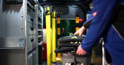 Arbeiter hebt einen Industriesauger in einem eingerichteten Servicefahrzeug