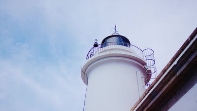 Weißer Leuchtturm ragt vor blauem Himmel an der Küste empor