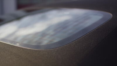 Gewölbte Kunststoffscheibe eines Cabrioverdecks spiegelt den bewölkten Himmel