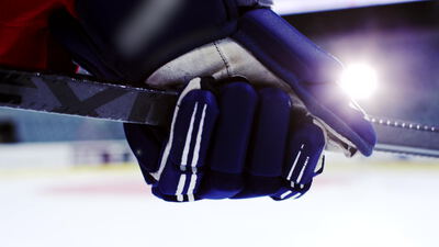 Behandschuhte Hand hält Eishockeyschläger im Gegenlicht
