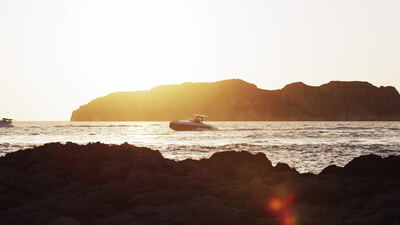 Kleines Motorboot passiert bei Sonnenuntergang eine Felseninsel
