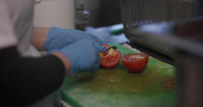 Behandschuhte Hände schneiden frische Tomate in der Gastronomieküche