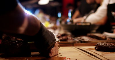 Koch schneidet gegrilltes Steak mit schwarzen Handschuhen auf einem Holzbrett
