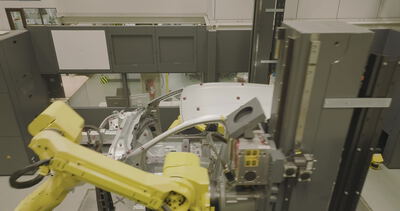 Gelber Industrieroboter handhabt eine Fahrzeugkarosserie in einer Messzelle