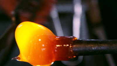 Glühendes Glas an der Glasmacherpfeife in der Werkstatt Glühendes Glas an der Glasmacherpfeife in der Werkstatt, Glasbläserei Nahaufnahme, flüssiges Glas und Glasposten am Rohr als