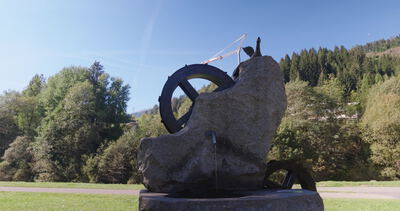Steinbrunnen mit zwei Rädern in Untersicht unter belaubten Zweigen