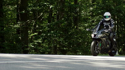 Motorradfahrer auf einem Sportmotorrad fährt über eine Waldstraße