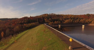 Drohnenflug über die Staumauer einer Talsperre im Herbstwald