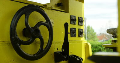 Schwarzes Handrad an einer gelben Maschine mit Schalthebeln: Handrad Maschine, schwarzes Speichenrad