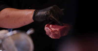 Behandschuhte Hand drückt frisches marmoriertes Ribeye Steak auf dunkler Fläche
