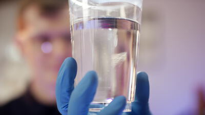 Behandschuhte Hand hält Glas mit reinem Wasser