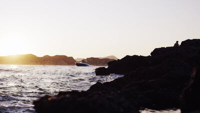 Person sitzt bei Sonnenuntergang auf Felsen und blickt aufs Meer