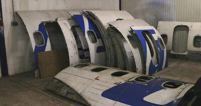 Blau weiße Flugzeugrumpfsektionen stehen aufgereiht in einer Werkhalle