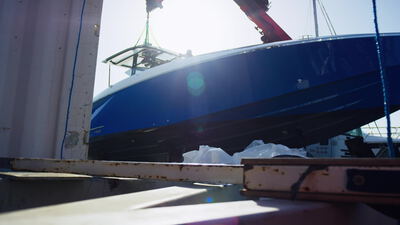 Blauer Yachtrumpf schwebt zwischen Kranstützen beim Zuwasserlassen