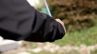 Hand hält einen weißen flachen Stab vor einer Gartenhecke