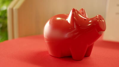 Rotes glänzendes Sparschwein auf roter Fläche vor grünem Hintergrund