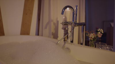 Schaumbad in der Badewanne mit Kerze und Blumen zu Hause