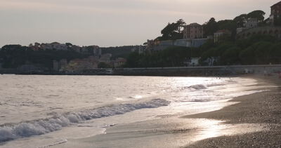 Wellen glitzern im Gegenlicht am Strand vor bebautem Hügel