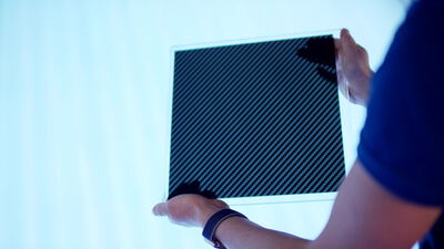 Hände halten transparente Platte mit Karbonfasergewebe