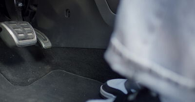Fuß im Sneaker nähert sich dem Bremspedal im Auto
