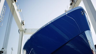 Glänzender blauer Bootsrumpf im Travellift vor strahlendem Himmel