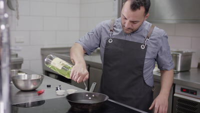 Koch gießt Olivenöl in eine Pfanne in der Restaurantküche