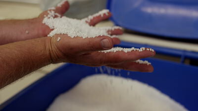 Hand lässt weißes Kunststoffgranulat über einen blauen Behälter rieseln Hand lässt weißes Kunststoffgranulat über einen blauen Behälter rieseln, Kunststoffkügelchen, Rohstoff und Kunststoffpellets