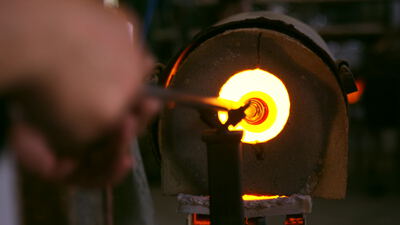 Glasbläser erhitzt Glasposten am glühenden Schmelzofen