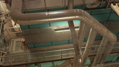 Isolierte Kanäle über einem Laufsteg vor türkiser Wand von unten gesehen
