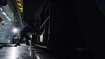 Arbeiter unter dem Bootsrumpf im Licht einer Werftlampe