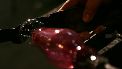 Handwerker formt rosafarbene Glaskugel mit einem Werkzeug, Christbaumkugel, Mundgeblasenes Glas und Weihnachtsschmuck als 4K