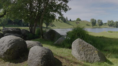 Felsbrocken säumen ein ruhiges Seeufer vor grünen Hügeln: Felsbrocken, große Felsbrocken