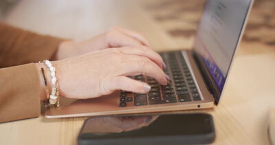 Weibliche Hände tippen auf der Tastatur eines rosegoldfarbenen Laptops