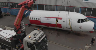 Roter Mobilkran hebt einen Flugzeugrumpf auf einen Lastwagen