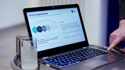Hand tippt am Laptop mit Unternehmenspräsentation auf Glastisch